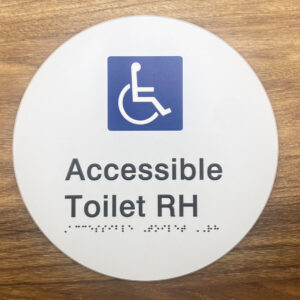 Photo of an Accessible Toilet RH on a White Acrylic Disk. White Disk with Blue & White International Symbol for Access, Black text that reads Accessible Toilet RH