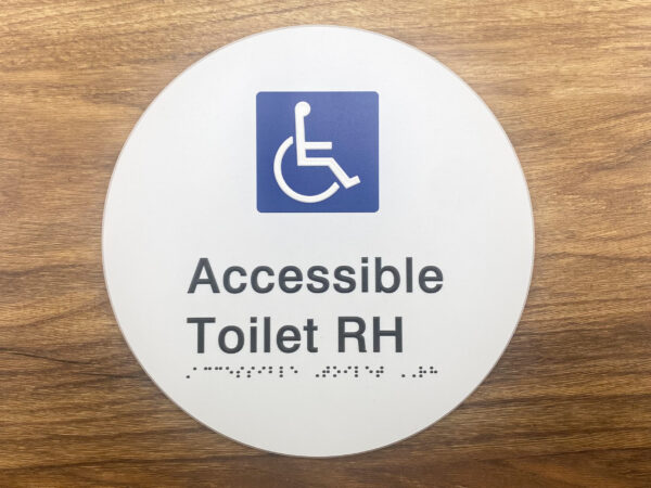 Photo of an Accessible Toilet RH on a White Acrylic Disk. White Disk with Blue & White International Symbol for Access, Black text that reads Accessible Toilet RH