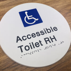 Photo of an Accessible Toilet RH Braille Sign. White disk with Blue & White international symbol for Access. Black text reads Accessible Toilet RH