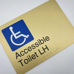 Accessible Toilet LH Braille Sign in Landscape Satin Brass. Brass Sign panel with Blue & White Accessible Symbol & Text that reads Accessible Toilet LH. Braille Text is shown