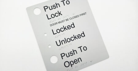 Push to Lock, Automatic Door Braille Sign in Anodised Aluminium. Silver sign panel with Black Raised text & Button holes. Braille is also shown