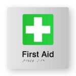 First Aid Braille Sign in Tactile Printed Silver Acrylic. Silver Sign panel with Green & White First Aid Symbol. Black Text reads First Aid. Black Braille Text is shown